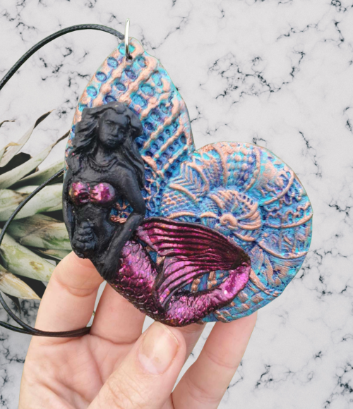 Whimsical mermaid resting on a giant seashell pendant on an adjustable cord made with polymer clay crafted by mouth